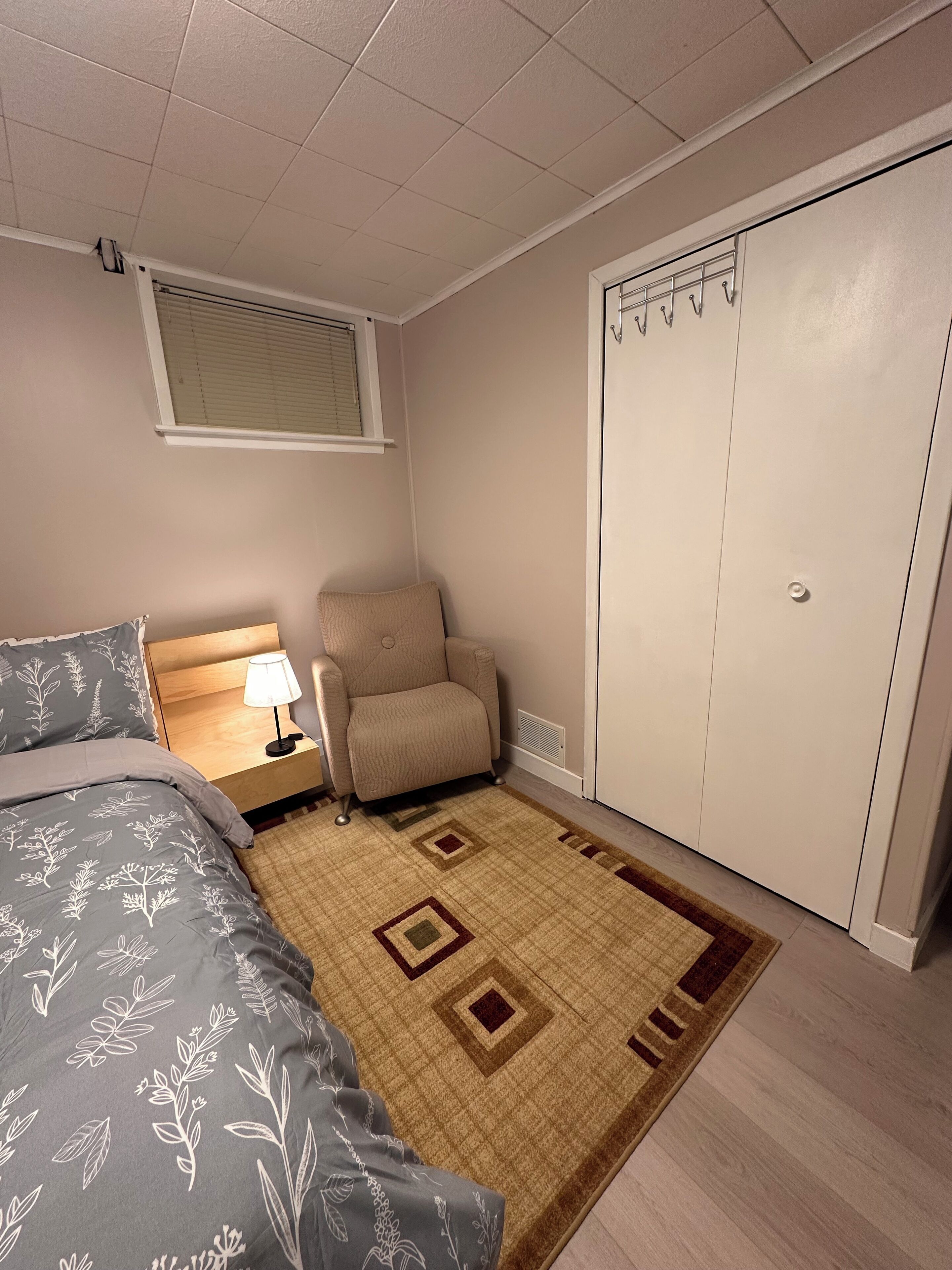 Ein Schlafzimmer mit Bett, Stuhl, Nachttisch, Kleiderschrank und Fenster mit Jalousien.