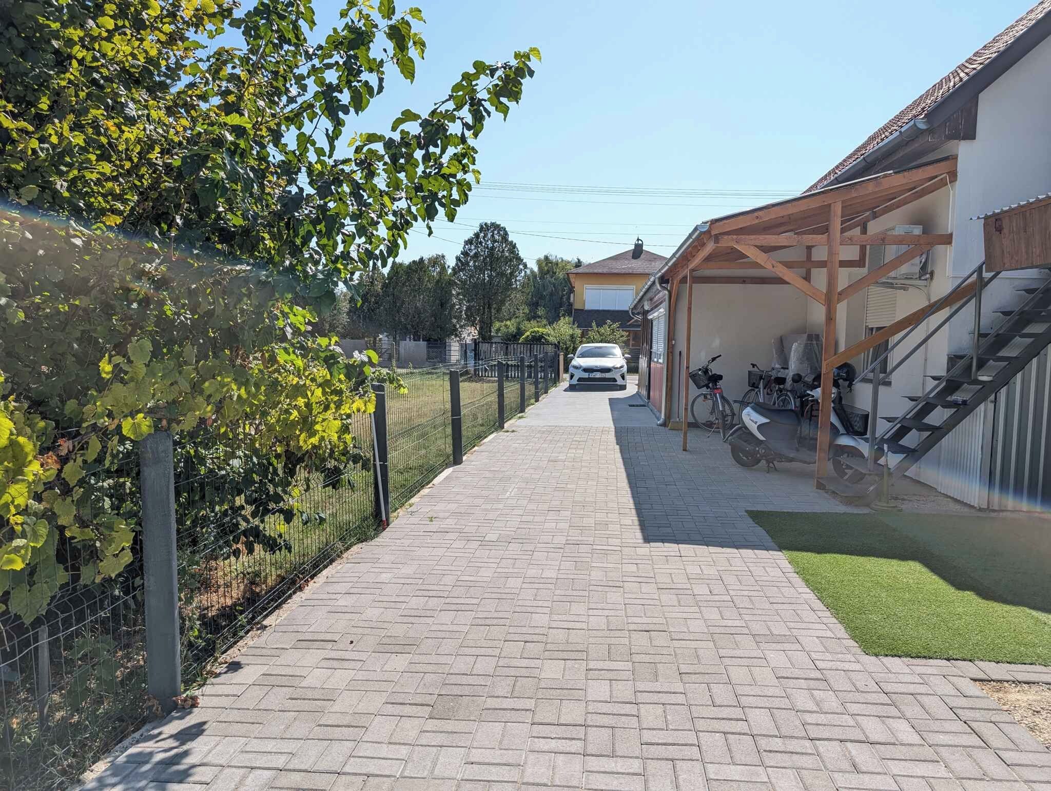 Un sendero pavimentado que conduce a un edificio con un porche cubierto, un coche aparcado y una bicicleta.