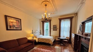 A bedroom with a bed, a sitting area with a table and chairs, a sofa, a fireplace, and a chandelier.