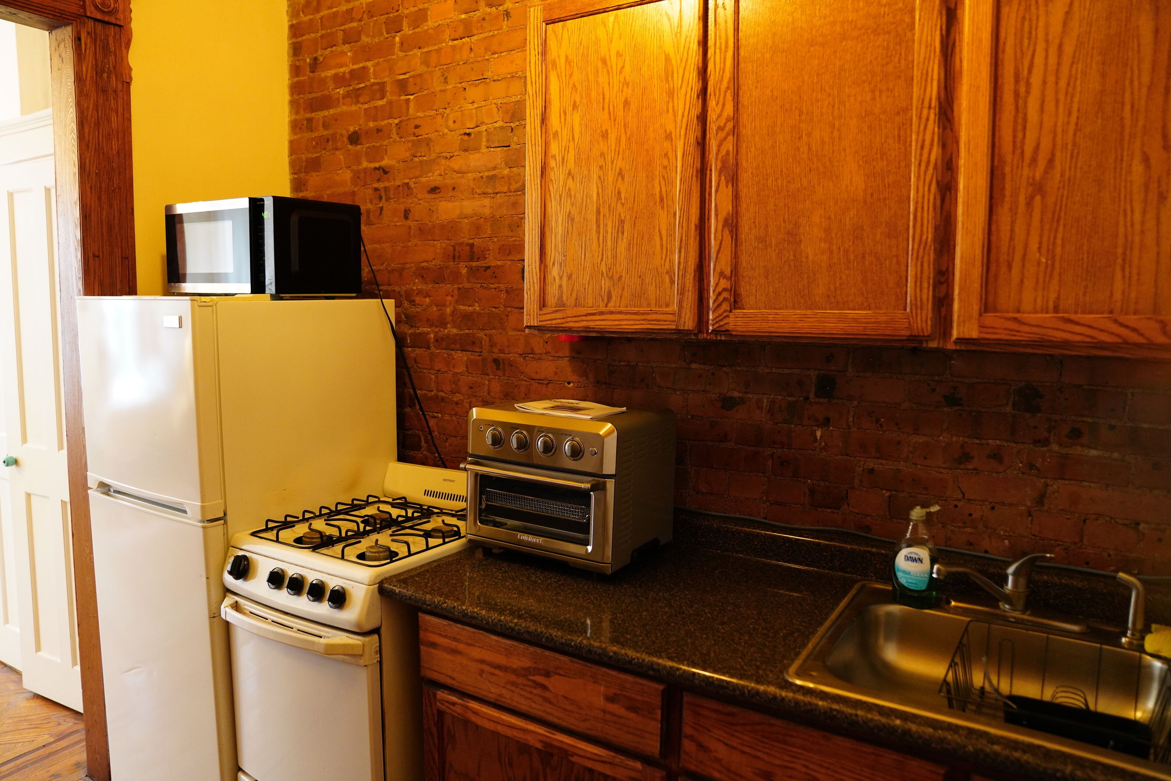 A kitchen with a gas stove, a microwave, a toaster oven, a refrigerator, wooden cabinets, and a sink.