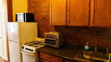 A kitchen with a gas stove, a microwave, a toaster oven, a refrigerator, wooden cabinets, and a sink.