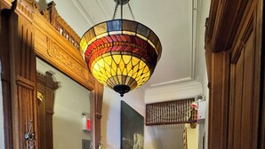 A hallway with wooden doors, a stained glass ceiling light, a painting on the wall, and a staircase in the background.