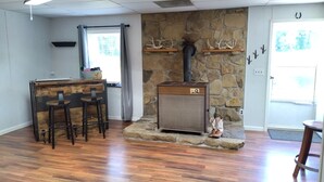 A room with a stone fireplace, a wooden bar area with stools, and a stone wall. - Charming Goat Farm in peaceful Hanson (Hanson)