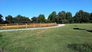 A fenced grassy area with a gravel path, surrounded by trees and a clear blue sky. - Charming Goat Farm in peaceful Hanson (Hanson)