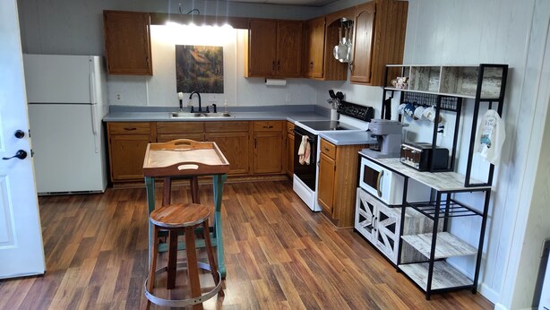 A kitchen with wooden cabinets, a white refrigerator, a sink, a stove, a coffee maker, and a shelf with kitchen utensils. - Charming Goat Farm in peaceful Hanson (Hanson)