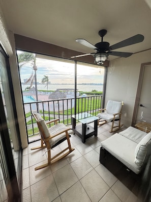 A balcony with a glass door, a ceiling fan, a pool, and a view of the water.