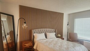 Une chambre à coucher avec une tête de lit capitonnée, un grand miroir, une lampe sur pied et une table de chevet.