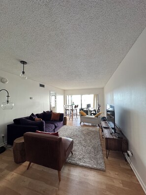 Un salon moderne avec un canapé, un fauteuil et un téléviseur posé sur un meuble en bois.