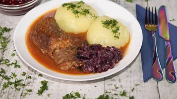 A plate with meat, potatoes, and red cabbage, accompanied by a fork and knife on a napkin.
