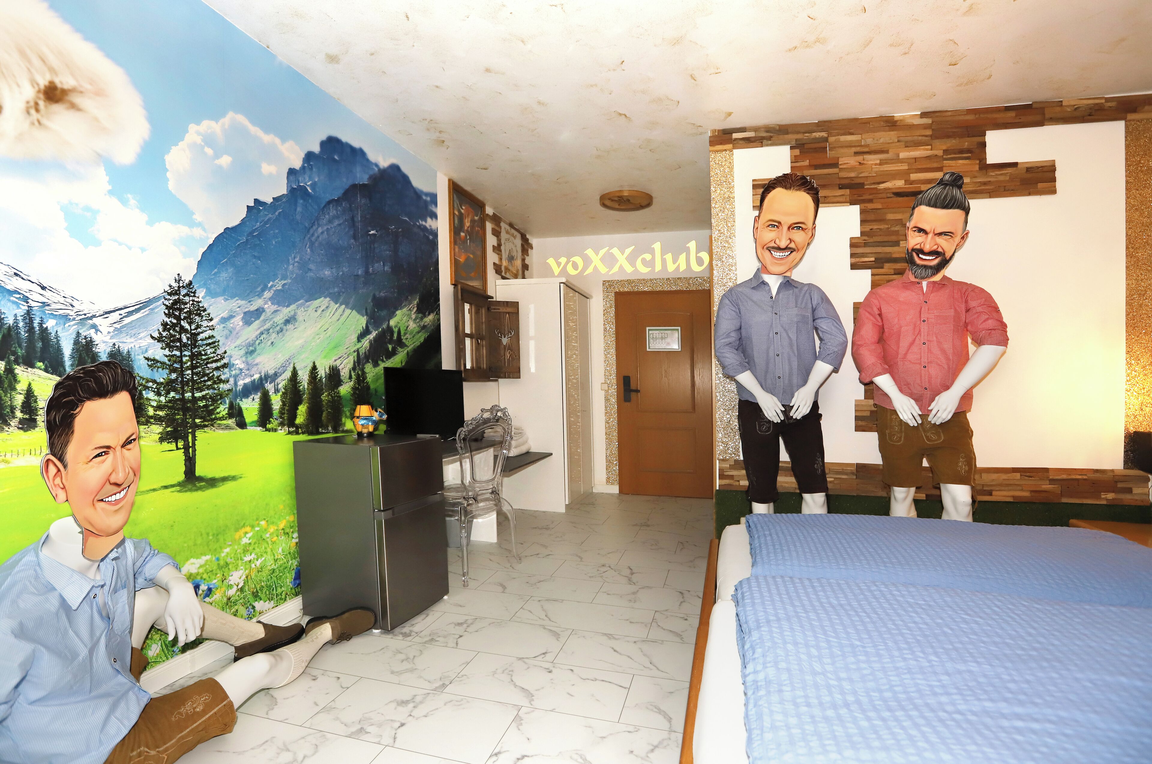 A room with a bed, a desk with a computer, a chair, a refrigerator, and a door.