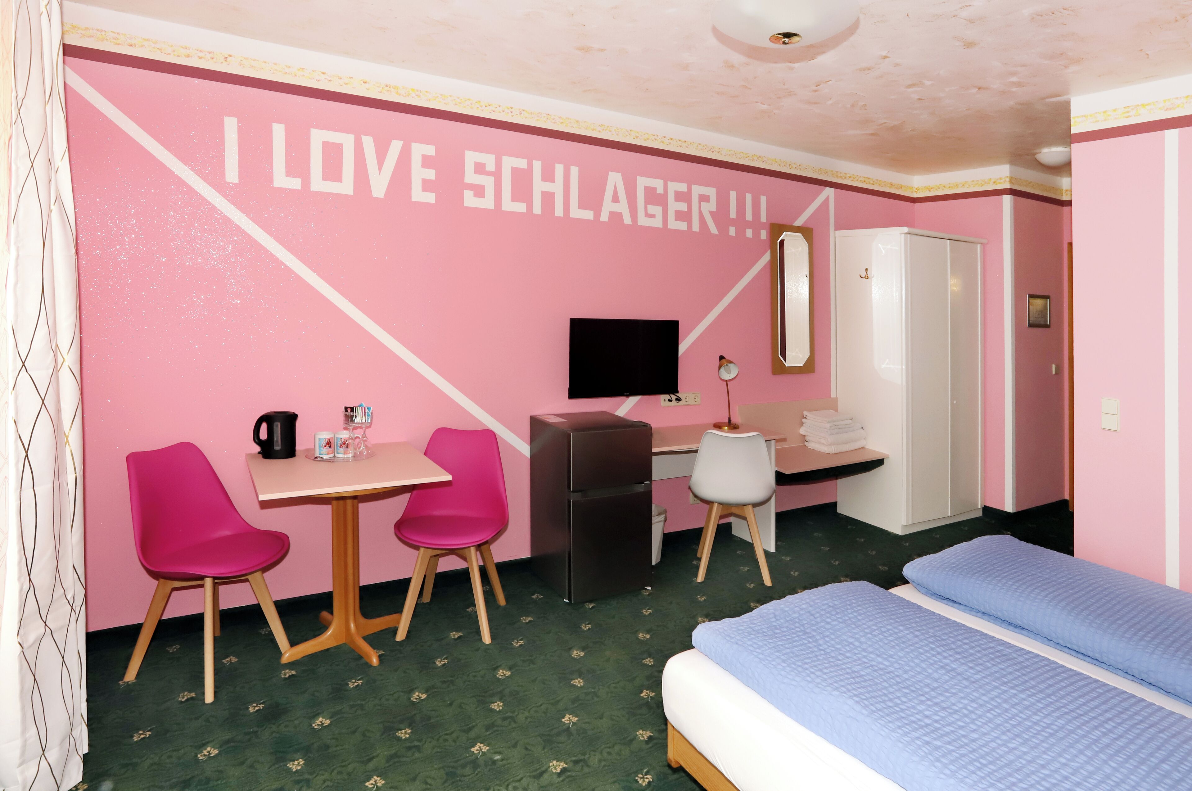 Camera d'albergo in tonalità rosa con un letto, una scrivania, sedie e una TV.