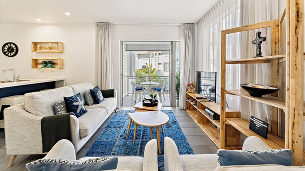 Een moderne woonkamer met een bank, salontafel en tv-meubel. Er is een balkon met een tafel en stoelen.