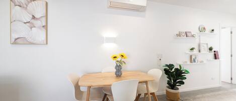 A dining area with a wooden table, white chairs, a vase with sunflowers, and a potted plant.