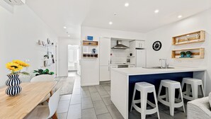 Een moderne keuken met witte kasten, een centraal eiland met krukken, en een eethoek met een houten tafel en stoelen.