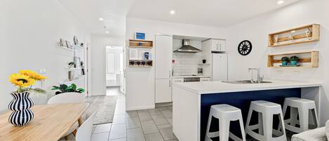 A modern kitchen with white cabinetry, a central island with stools, and a dining area with a wooden table and chairs.