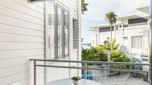 Een balkon met een ronde tafel en stoelen, een zwembadje en uitzicht op palmbomen en gebouwen.