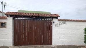 A large brown gate with a green roof, a white wall with a sign reading "El Portal", and a small window on the left.