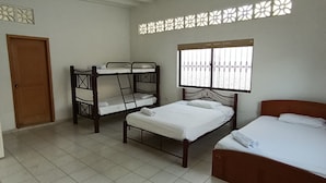 A room with two bunk beds, a single bed, a wooden door, and a window with decorative bars.