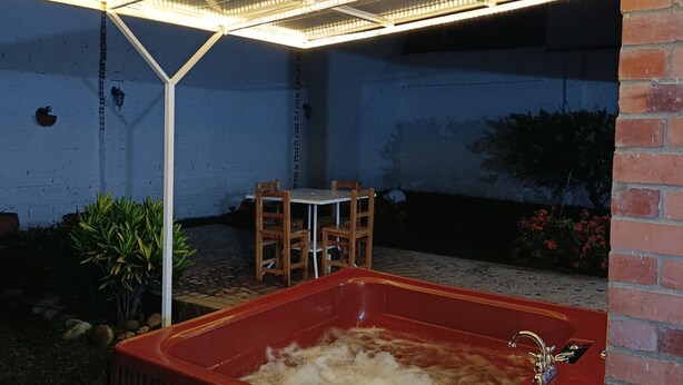 A hot tub under a covered patio with a brick wall and a small table and chairs in the background.