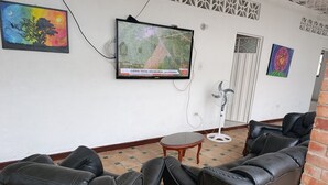 A room with black leather sofas, a small wooden table, a TV mounted on the wall, and a decorative painting.