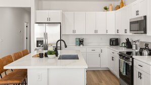 A modern kitchen with white cabinets, a central island, stainless steel appliances, and wooden chairs. - Lakeview Oasis at Powell - Heated Pool+Lake Views+Game Room (Page)