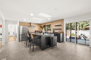 Una cucina moderna con isola centrale, sgabelli da bar, frigorifero in acciaio inox e pannello di rivestimento in legno.