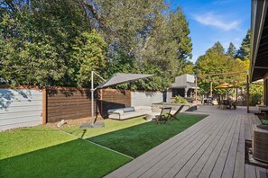 Un patio trasero con terraza de madera, un pequeño espacio de estar con mesa y sillas, y un porche cubierto.