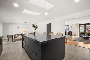 A modern kitchen with a large island, dining area, and a view into the living room.