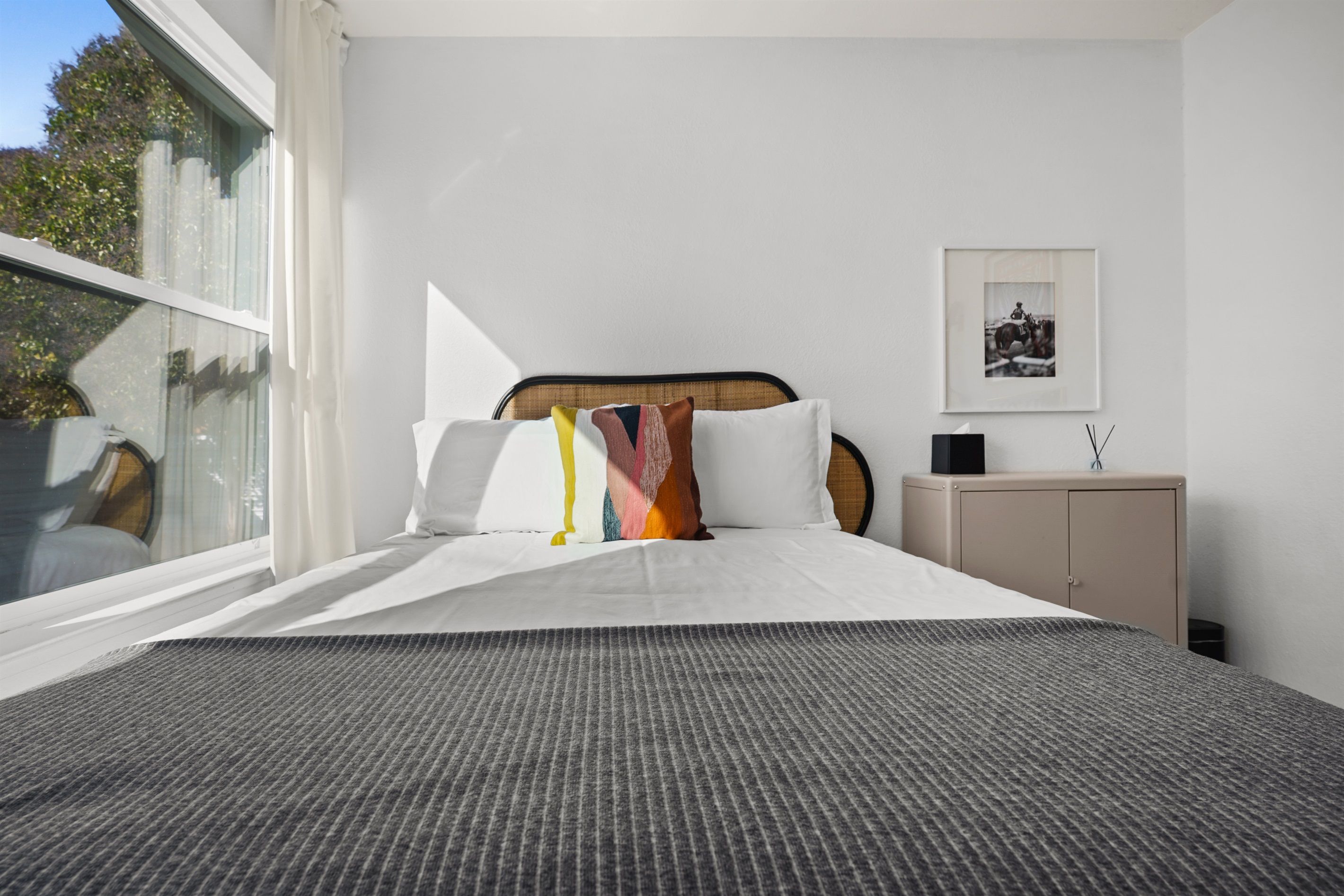 Quarto com cama, mesa de cabeceira, quadro na parede e janela com cortinas.