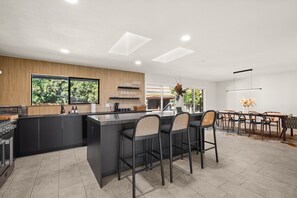 A modern kitchen with a central island, bar stools, and a dining area with a table and chairs.