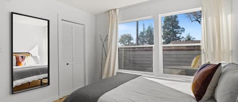 Ein Schlafzimmer mit einem Bett, einem Fenster mit Vorhängen, einem Spiegel und einem Kleiderschrank.