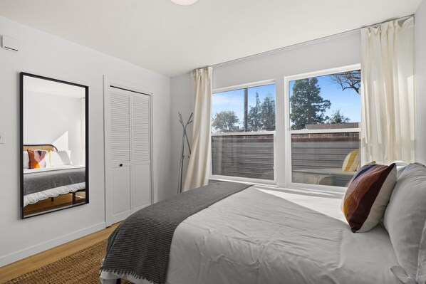 Un dormitorio con cama, ventana con cortinas, espejo y armario.