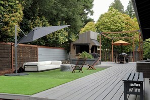 A patio with a wooden deck, a white sofa, and a grill area.