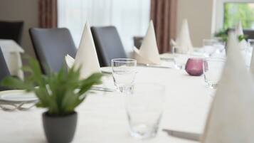 A dining table set with white napkins, clear glasses, and a potted plant.