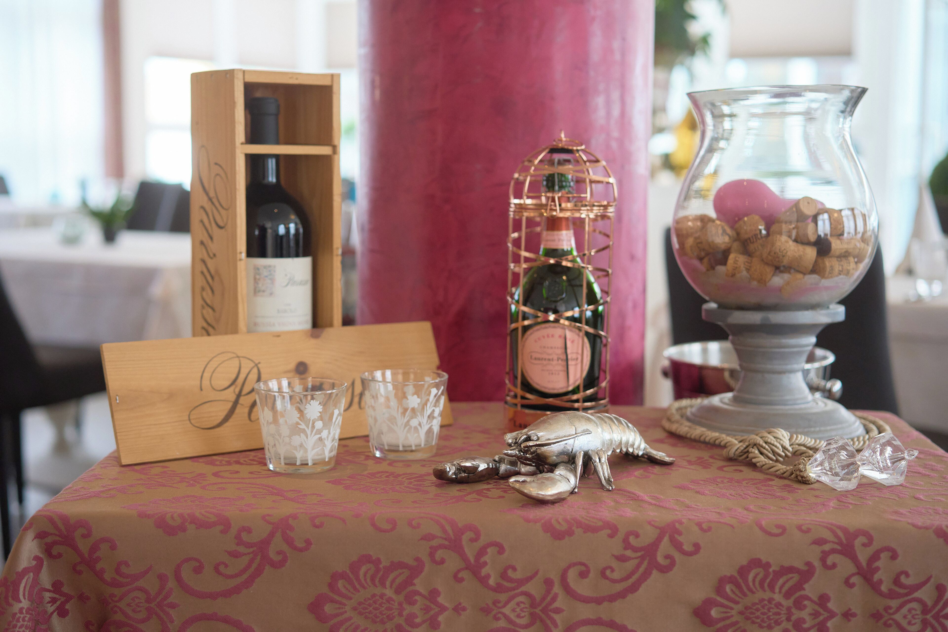 Uma mesa com uma placa de madeira, uma garrafa de champanhe, um pote com rolhas e uma decoração de lagosta.