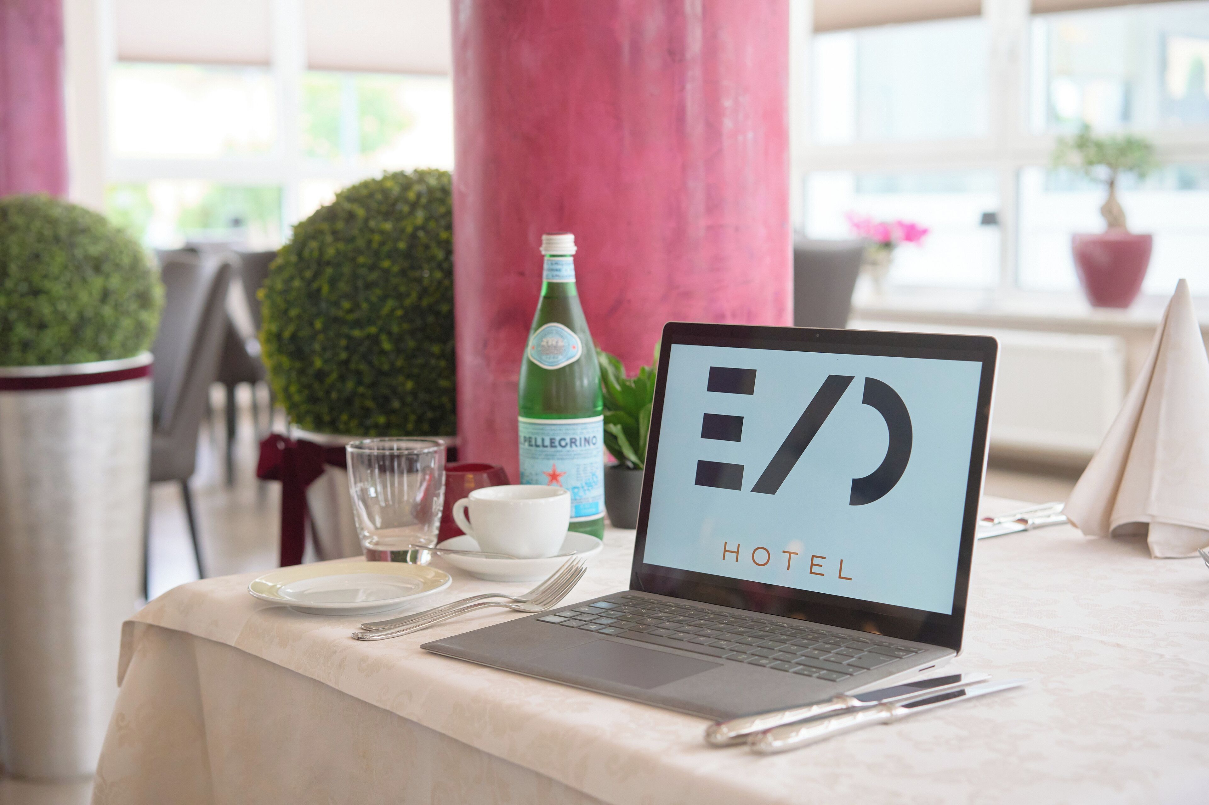 A laptop on a table with a glass of water, a cup, and a bottle of Pellegrino water.