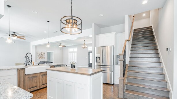 A spacious kitchen with a large island, stainless steel appliances, and a wooden staircase.