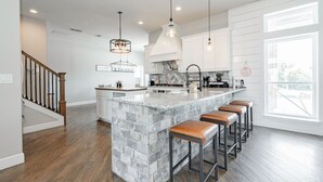 A modern kitchen with a large island, bar stools, pendant lighting, and a view to the outside.