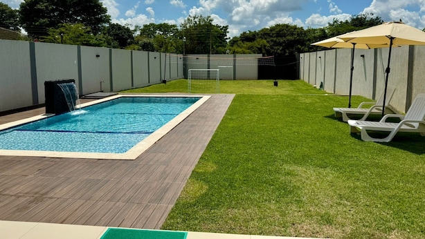 A backyard with a swimming pool, a grassy lawn, and a volleyball net.