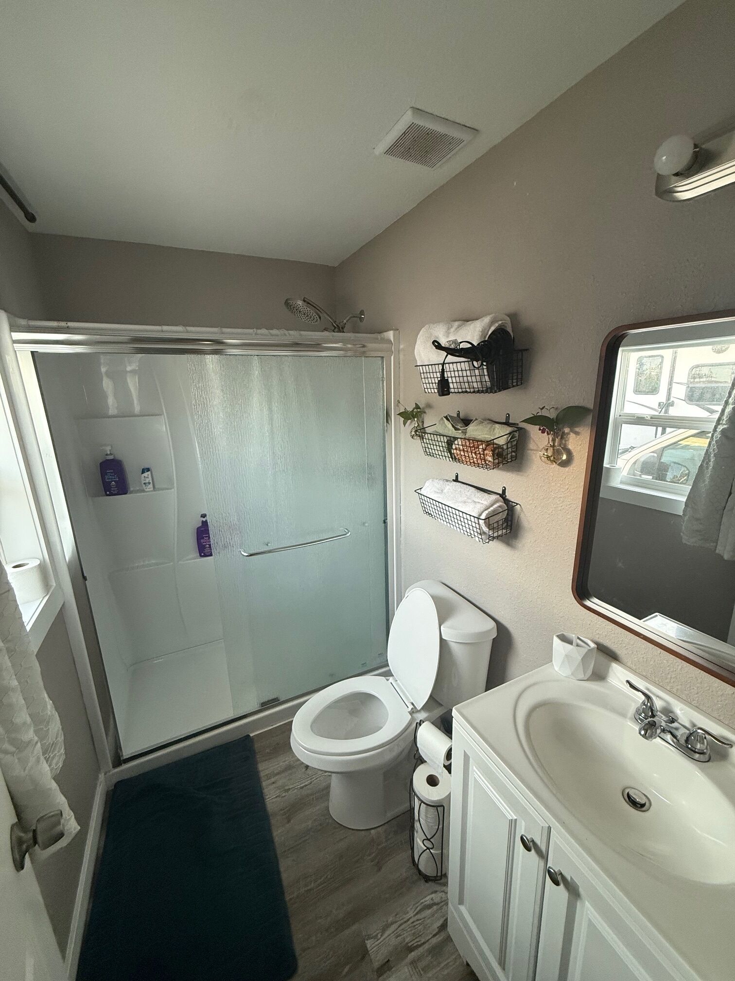 A bathroom with a shower, toilet, sink, and a mirror.