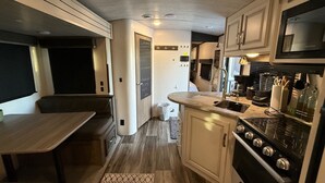 Cocina compacta para vehículos recreativos, con estufa, fregadero y una pequeña zona de comedor.