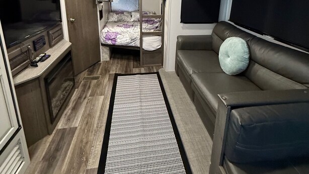 Interior compacto de autocaravana con kitchenette, cama, zona de estar y televisor.