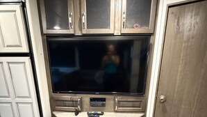 Una cocina con una televisión de pantalla plana grande, armarios de madera y un microondas integrado.
