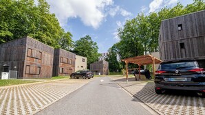 A street with a paved walkway, parked cars, and wooden buildings. - Maison Marguerite - Welkeys (Bayonne)