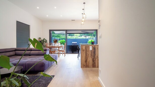 A modern living room with a sectional sofa, a dining area with a table and chairs, and a kitchen area with a wooden counter. - Maison Marguerite - Welkeys (Bayonne)