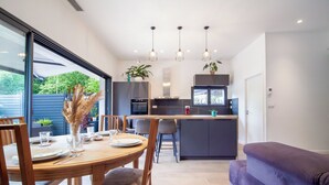 A modern kitchen with a dining area, featuring a wooden table, chairs, and a purple sofa. - Maison Marguerite - Welkeys (Bayonne)