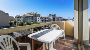 Un balcon avec une table et des chaises, donnant sur un paysage urbain avec des bâtiments et un ciel dégagé.