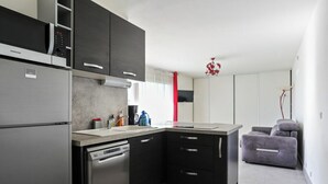Une cuisine moderne équipée d’un lave-vaisselle, d’un four à micro-ondes et d’un four encastré. Le salon est agrémenté d’un rideau rouge et d’un canapé gris.