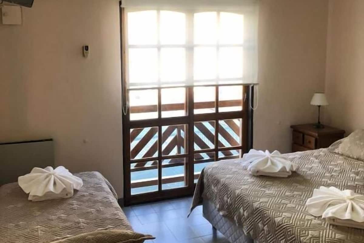 A hotel room with two beds, a ceiling fan, a TV, and a window with a view.