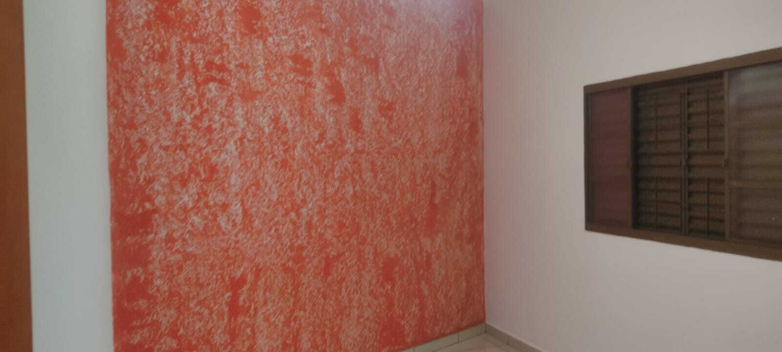Ein Zimmer mit einer strukturierten roten Wand, einem Fenster mit Jalousien und einem gefliesten Boden.